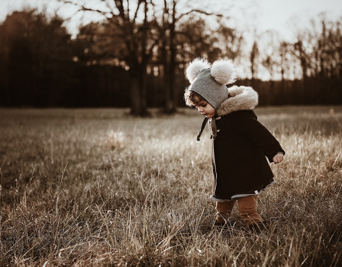 baby girl in winter bonnet in brimless pom bonnet in frosty field at sunset